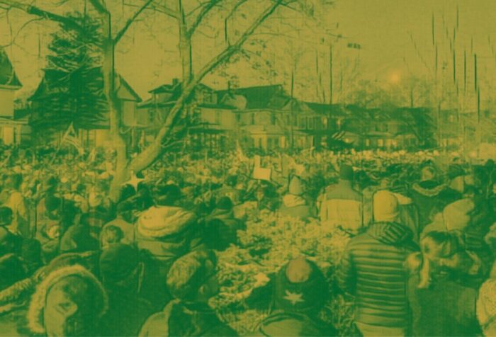 A crowd of people fills a street of houses with their backs to the camera. Photo has a green filter over it.