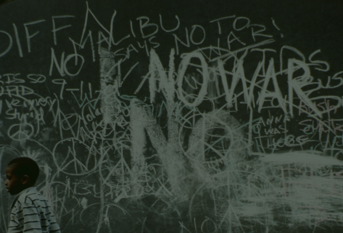 A photo of a wall covered in anti-war graffiti. A child walks in front of it.