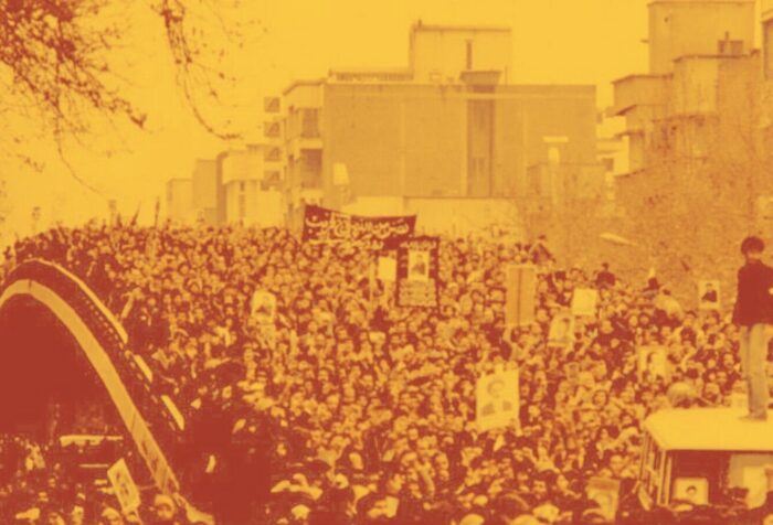 An orange-tinted photo of a protest crowd across a bridge holding signs in Persian.