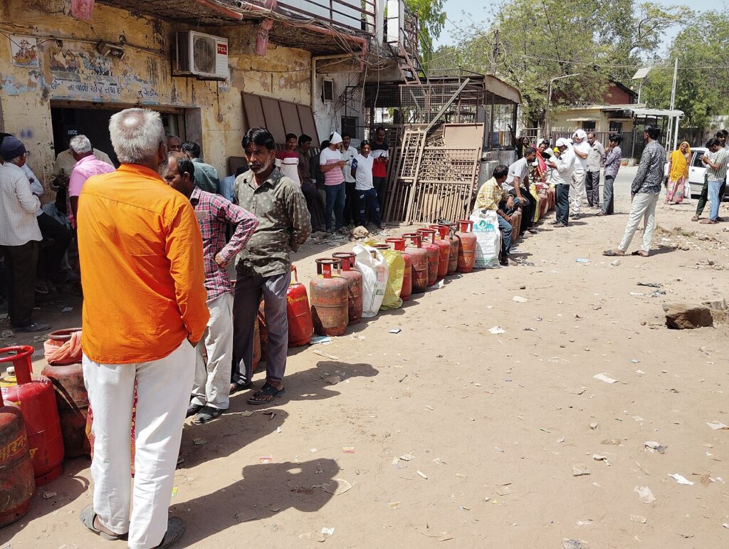 People standing in bright sunshine on a dirt path alongside of a row of red metal cylinders.