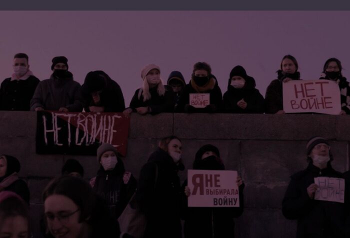 People standing in a line behind a wall holding signs.