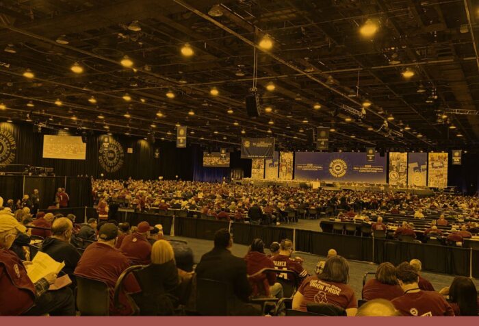 An audience of people sitting in a convention hall with UAW signs.