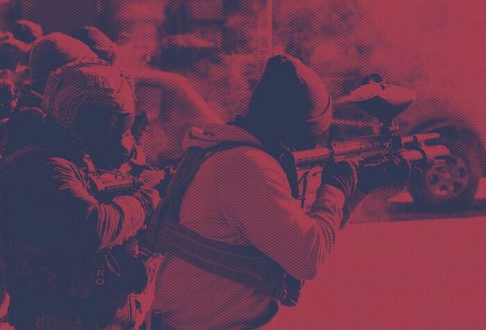 A red-tinted photo of ICE officers shooting non-lethal rounds.