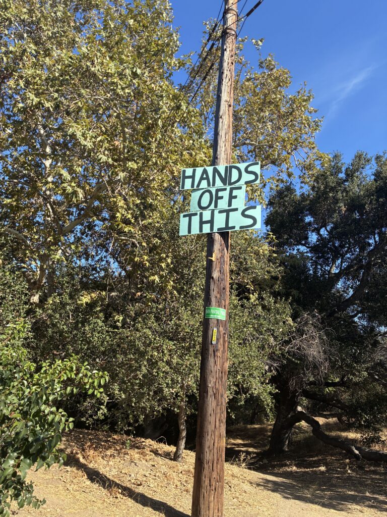 A sign saying "hands off this" on a pole in San Pascual Park.